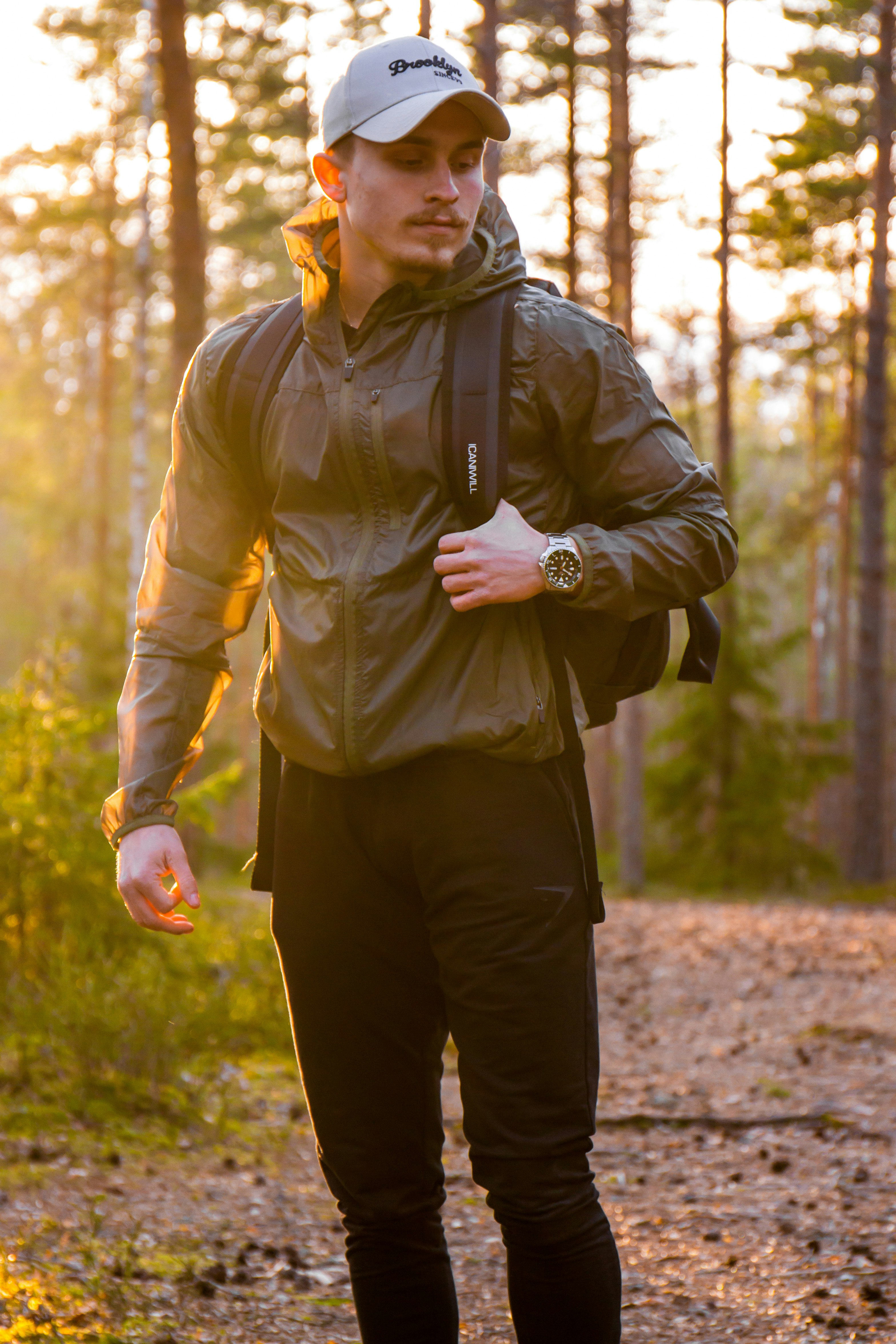 man in green jacket and black pants standing on forest during daytime